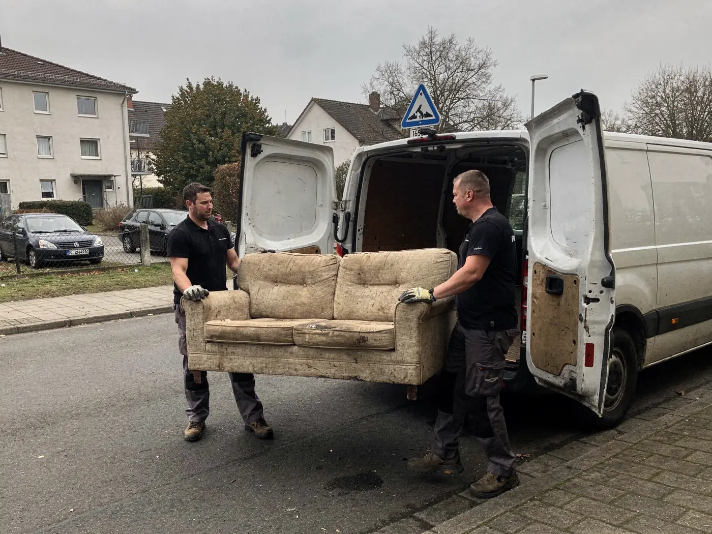 Zwei Mitarbeiter heben ein altes Sofa in den Transporter.